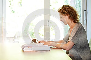 Happy woman sitting at table working on laptop