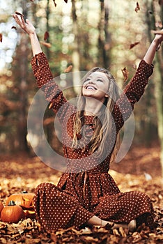 Happy woman sitting and throwing autumn leaves in the forest