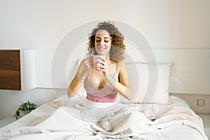Happy woman in sleepwear looking at coffee cup while sitting in bed