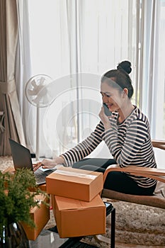 Woman small business owner receive order on smart phone and writing address on cardboard box.