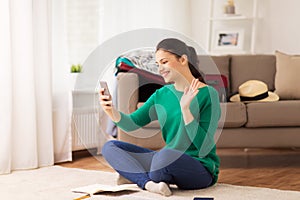 Happy woman with smartphone waving hand at home