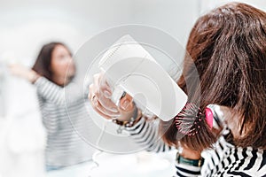 Happy woman smiling and drying her hair with hairdryer near the mirror in the bathroom