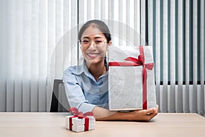Happy woman is smiling and holding big present box with red ribbon in the hands while preparing gift for celebrate