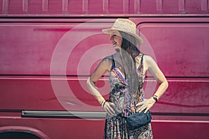 happy woman smiling standing, looking in profile, wearing hat and colorful dress and van in background