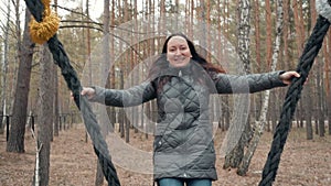 Happy woman smiling while swinging in autumn forest. Cheerful woman having fun on forest swing and looking to camera