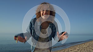 Happy woman smiling turning on camera on beach close up. Curly girl waving hands