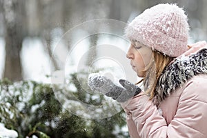 Happy woman on a snowy winter day in the park,dressed in warm clothes, blows the snow off her mittens