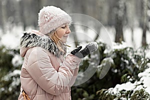 Happy woman on a snowy winter day in the park,dressed in warm clothes, blows the snow off her mittens