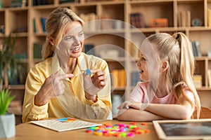 Happy woman speech therapist teaching little girl with pronounciation deffects to say sound R during personal training