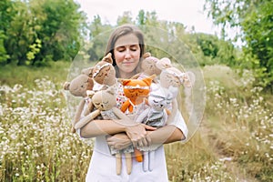 A happy woman stand in a green meadow with a set of soft toys cats. Girl hugs a set of toy cats in hands