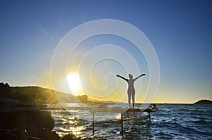 Happy woman standing arms outstretched back and enjoy life on the beach pier at sunset