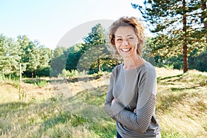 Happy woman standing in countryside with arms crossed