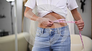Happy woman standing in front of the mirror in jeans is measuring waist after lost weight