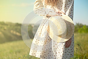 Happy woman standing with her back at the edge of a mountain cliff at sunset light sky holding a straw hat
