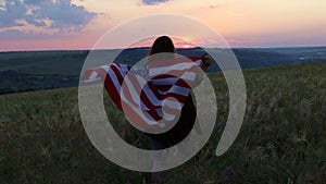 Happy woman standing with her back on sunset in nature iwith open hands with USA flag