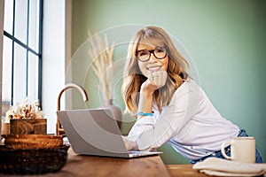 Happy woman standing in the kitchen and using her laptop