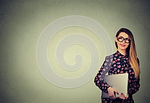 Happy woman standing with laptop over gray wall background