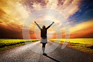 Happy woman standing on long road at sunset