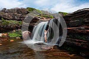 Happy woman standing under a waterfall in bushland wilderness