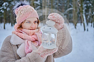 A happy woman stands with a lantern in her hands, a winter park with snow-covered trees