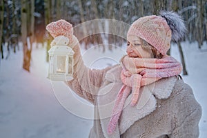 A happy woman stands with a lantern in her hands, a winter park with snow-covered trees