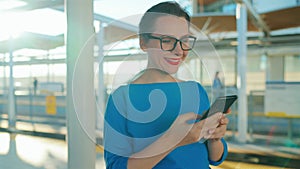 Happy woman stands at a public transport stop and chatting on smartphone