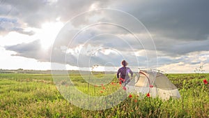 Happy woman stands on sunset flower field near travel tent with her hands up