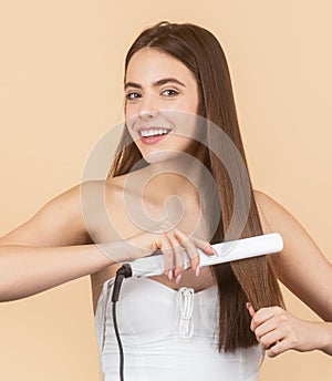 Happy woman straightening hair with straightener. Portrait of young beautiful girl using styler on her shining hair