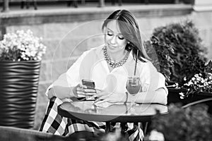 Happy woman in a street cafe reading a text message from her phone. Female making on-line shopping with internet on mobile phone