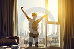 Happy woman stretches and opens curtains at window in morning