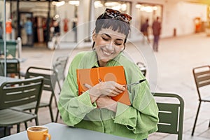 happy woman student writing in a notebook, making plan at the street cafe in city. Concept of study hard Lifestyle photo