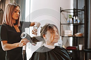 Happy woman with stylist making hairdo at salon