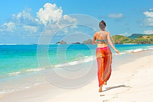 Happy woman in summer loose trousers running on tropical beach photo