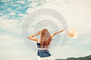 Happy Woman in summer vacation holding hat and wearing dress enjoying the view at the island beach