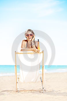 Happy woman with suntan lotion sitting in beach chair