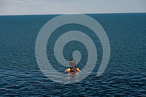 Happy woman in swimsuit swimming in infinity pool against seafront.