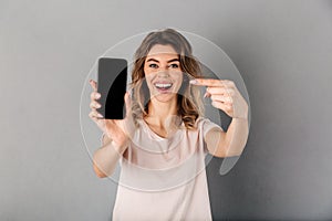 Happy woman in t-shirt showing blank smartphone screen