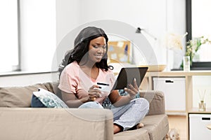 Happy woman with tablet pc and credit card at home