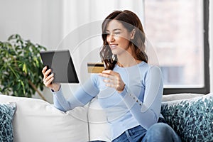 happy woman with tablet pc and credit card at home