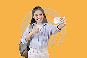 Happy woman taking selfie with phone on yellow background