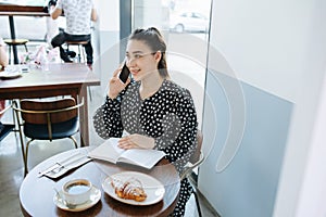 Happy woman talking on the phone in a cafe. Sitting behind round table