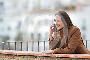 Happy woman talks on phone in a balcony in winter