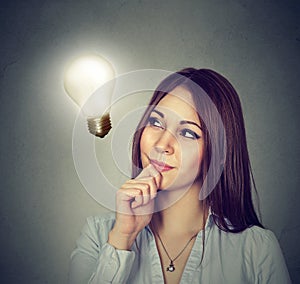 Happy woman thinking looking up at bright light bulb