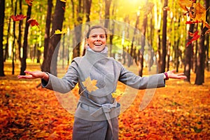 Happy woman throwing leaves around on an autumns day. Autumn leaves falling on happy young woman in colourful forest park.