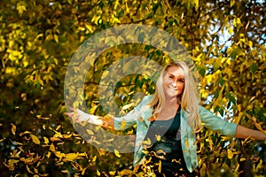 Happy woman throwing up leaves in autumn, smiling. A joyful and excited young woman happily throws yellow leaves in a