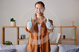 Happy woman, thumbs up and cleaning service with a smile in a house or apartment living room for safety with gloves
