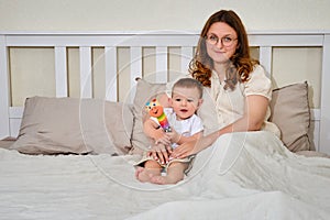 Happy woman with a toddler baby in an empty bed. Smiling mother wit