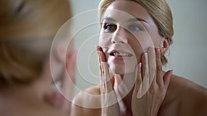 Happy woman touching face, good effect of anti aging lotion, daily skincare