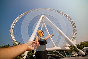 Happy woman tourist making follow me pose at Ain Eye DUBAI - One of the largest Ferris Wheels in the World, located on