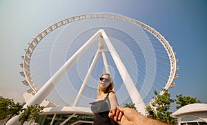 Happy woman tourist making follow me pose at Ain Eye DUBAI - One of the largest Ferris Wheels in the World, located on